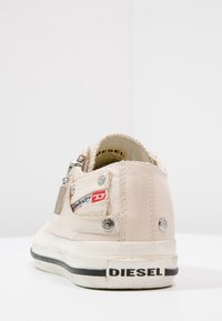 Sneaker in pelle beige con superficie texturizzata, dettagli in metallo argentato, suola bianca con striscia nera e logo del marchio sul tallone.