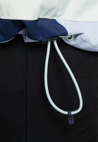 Jasnoniebieska kurtka z granatowym obszyciem, wyposażona w sznurek ze ciemnym zaciskiem. Gładka tekstura z ściągaczem na dole dla dopasowanego wyglądu.