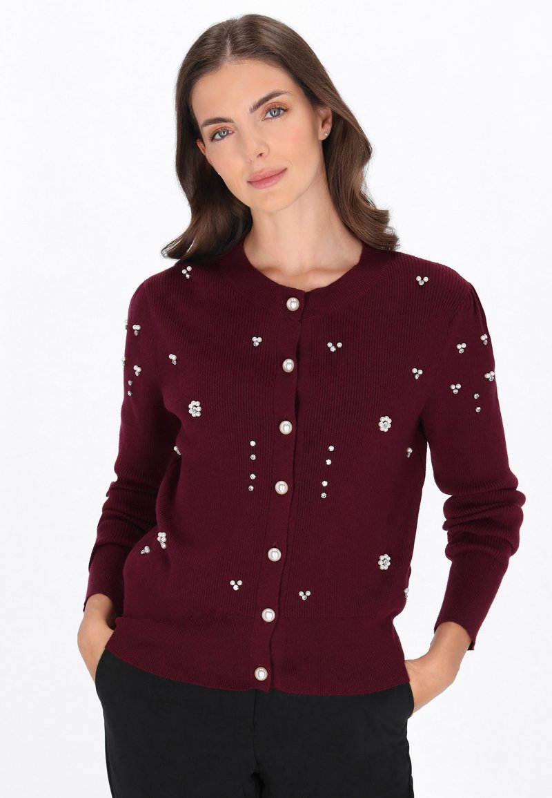 Burgundowy kardigan z okrągłym dekoltem, ozdobiony perłowymi akcentami i małymi dekoracjami kwiatowymi. Tekstura w prążki i zapięcie na guziki.