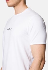 Biała bawełniana koszulka z okrągłym dekoltem i krótkimi rękawami, z małym czarnym logo "LANCERTO" po lewej stronie klatki piersiowej.