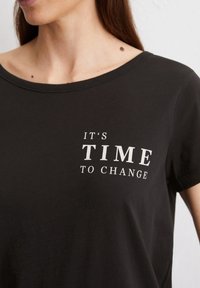 Schwarzes Kurzarm-T-Shirt aus Baumwolle mit weißem Text auf der Vorderseite, der "ES IST ZEIT ZU ÄNDERN" lautet.