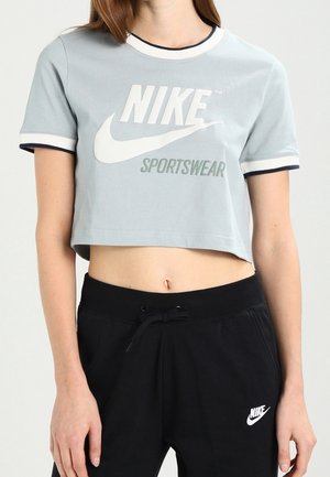 Persona que lleva una camiseta corta azul claro de Nike Sportswear y pantalones deportivos negros de Nike con cintura ajustable con cordón.