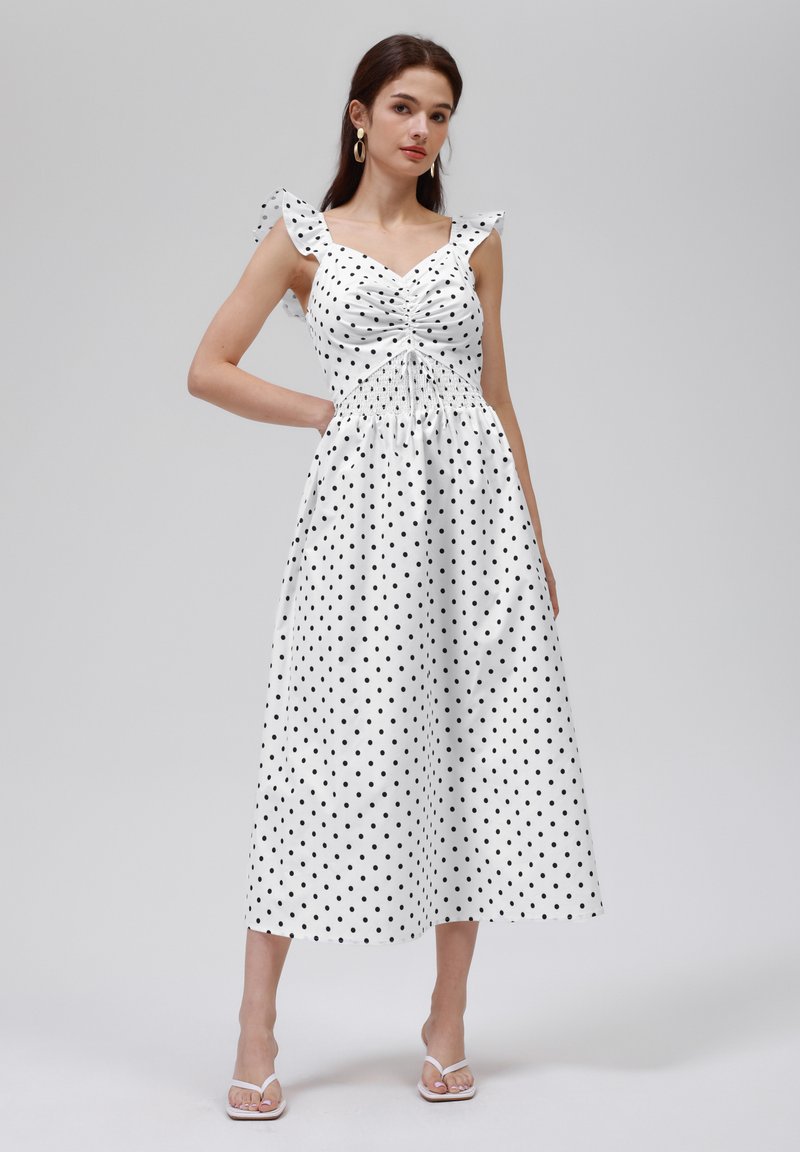 Midikleid mit Polka-Dots in Weiß und Schwarz. Verfügt über ein tailliertes Oberteil, Rüscheträger und einen gerafften Taillenbereich mit einem fließenden Rock.