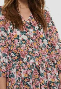 Mujer con un vestido floral con flores rosas, blancas, amarillas y verdes, con escote en V abotonado y mangas tres cuartos.