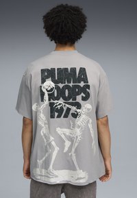 Camiseta de algodón gris con gran texto negro y un gráfico de esqueleto blanco en la parte posterior, que representa a dos esqueletos jugando baloncesto.