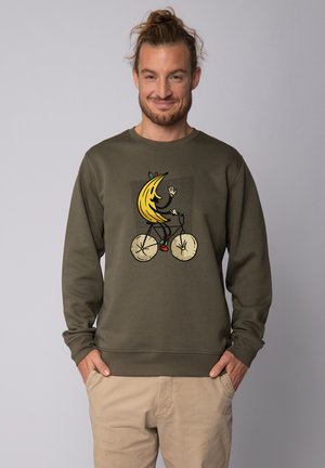 Olive green sweatshirt with a round neck. Features a central graphic of a banana character riding a bike, with beige accents and black outlines.