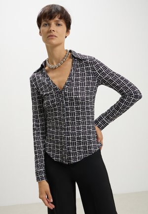 Camicia button-up colorate in bianco e nero con pattern geometrici. Presenta maniche lunghe e una silhouette aderente, abbinata a pantaloni neri.