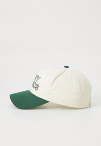 Căciulă de baseball cu un corp din bumbac crem, vizor verde și text brodat în verde închis. Dispune de un buton pe partea de sus și găuri de ventilație.