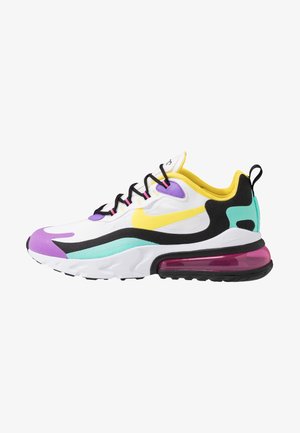 Zapatilla deportiva blanca con detalles en amarillo, morado, azul verdoso y negro, cordones negros y suela visible con cámara de aire rosa sobre fondo blanco.