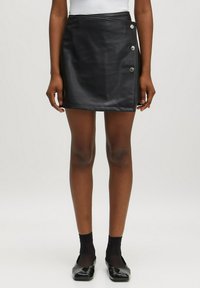 Zwarte faux leren minirok met een wikkelontwerp, voorzien van zilveren knoopaccenten aan de zijkant, een gladde textuur en een getailleerde silhouet.