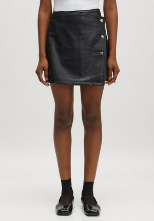Zwarte faux leren minirok met een wikkelontwerp, voorzien van zilveren knoopaccenten aan de zijkant, een gladde textuur en een getailleerde silhouet.