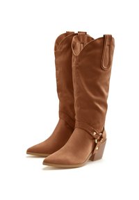 Botas de vaquero de ante marrón hasta la mitad de la pantorrilla con puntas afiladas, correas decorativas y pequeños accesorios en dorado. Cuentan con un tacón apilado para mayor estabilidad.