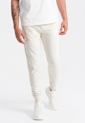 Pantalones jogger crema confeccionados en una tela suave, con un corte ajustado, puños acanalados y bolsillos laterales, combinados con zapatillas blancas.