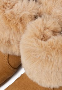 Brune ruskindsstøvler med en fluffy beige pelskant. Pelsen er tæt og blød, hvilket øger varme og komfort. Synlige sømme på ruskindet.