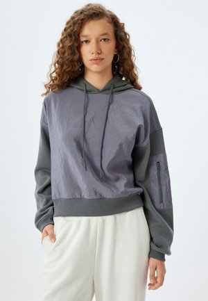 Sudadera con capucha de diseño bicolor: tela gris y lavanda apagada, con frente texturizado, dobladillo acanalado y bolsillo con cremallera en la manga.