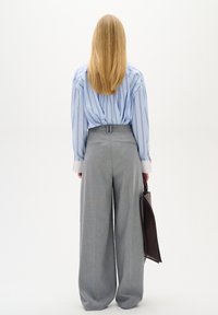 Mėlynai ir baltai raižytas ilgomis rankovėmis marškiniai, įsuktas į aukšto juosmens pilkus plačius kelnes, laiko rudą rankinę. Lygus paviršius, pritaikytas siluetas.