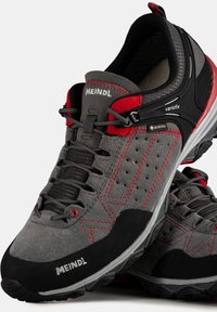 Szare zamszowe buty trekingowe z czerwonymi akcentami, wodoodporną podszewką Gore-Tex, wzorzystą gumową podeszwą oraz regulowanym systemem sznurowania.