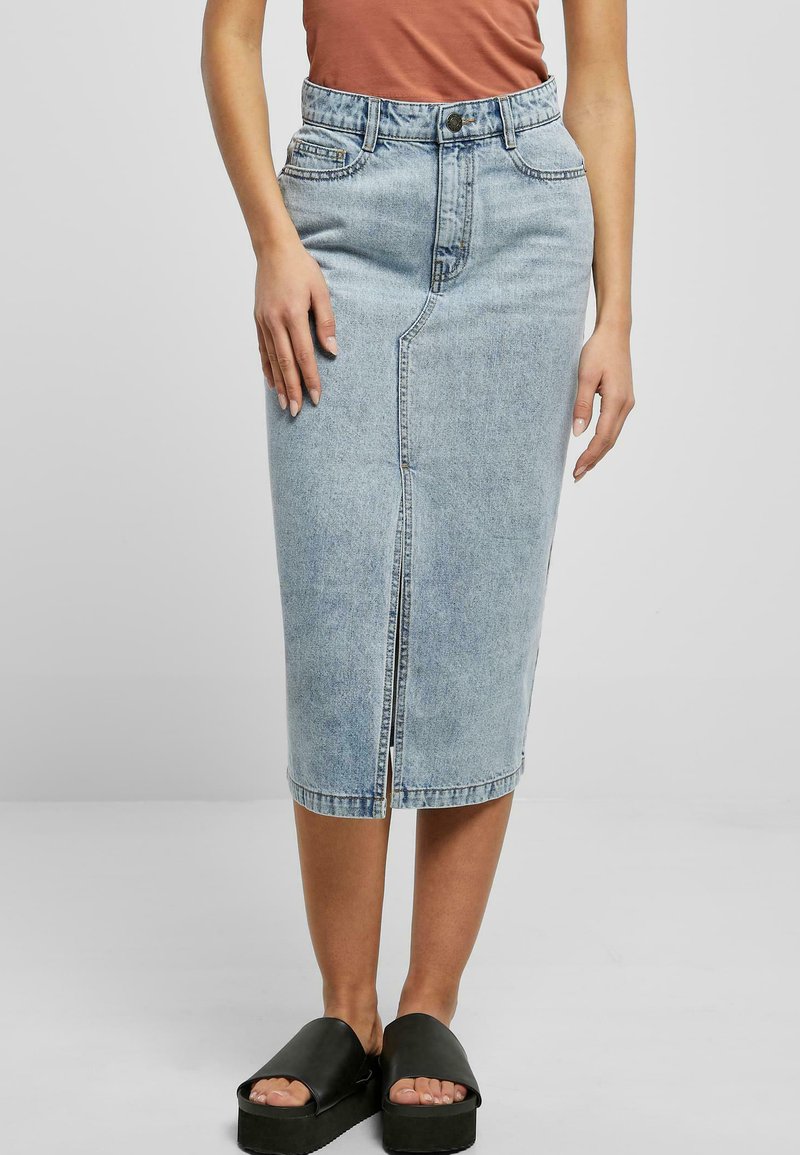 Lys blå denim midi-skjørt med frontslitt, høy liv, og fem lommer. Kombinert med svarte platåsandaler. Glatt tekstur.