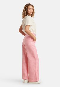 Pink wide-leg trousers with a textured weave, high waist, and loose fit, paired with a white eyelet blouse and white sneakers.