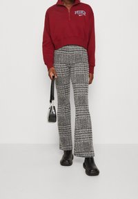 Burgundy kort sweatshirt med dragkedja och logotyp. Svarta och vita mönstrade utsvängda byxor. Svart texturerad handväska. Svarta ankelstövlar.
