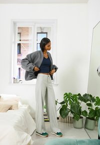Grå oversized bomberjacka, marinblå crop top, ljusgrå vida byxor, gröna sneakers med vita och rosa detaljer, inomhusväxter i krukor.