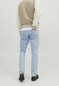 Ljust blå jeans med slim fit, parat med en beige och vit varsityjacka med randiga ärmslut och bakdetaljer. Bruna skor.