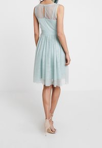Světle tyrkysové šaty s upnutým živůtkem a rozšířenou sukní. Bez rukávů s průhlednými panely na ramenou a detaily ve tvaru klíčové dírky na zadní straně.