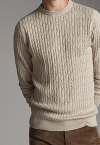 Kermanvärinen palmikkoneulepaita pyöreällä pääntiellä sekä resorilla varustetut hihansuut ja helma, jossa kauttaaltaan kohokuvioitu kuvio.