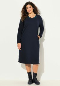 Laivaston sininen pitkähiha dressi V-kaula-aukolla, jossa on teal-väriset yksityiskohdat kaula-aukossa, sivutaskut ja rento istuvuus. Yhdistetty mustiin nauhakengiin.