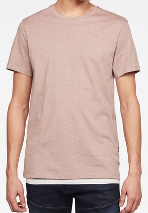 Homme portant un t-shirt à manches courtes marron clair uni par-dessus un sous-vêtement blanc avec un jean bleu foncé, montré des épaules aux hanches.