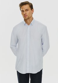 Jasnoniebieska koszula z długim rękawem z małym wzorem, zapinana na guziki z klasycznym kołnierzykiem i zaokrąglonym dołem, w połączeniu z ciemnymi dżinsami.