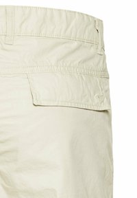 Lys beige bomuldsshorts med en baglomme. Stoffet har en glat overflade og let rynkning, med en syet talje.