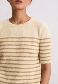 Krótki sweter z krótkim rękawem w kolorze kremowym z naprzemiennymi beżowymi paskami, z okrągłym dekoltem i teksturowaną, miękką tkaniną. Bezszwowe rękawy zwiększają komfort.