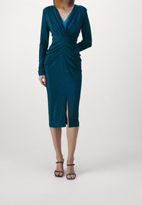 Teal, långärmad klänning med djup V-ringning, rynkdetaljer vid midjan och en framspalt. Tillverkad av ett glänsande, strukturerat tyg.