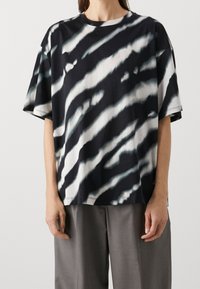 Camiseta de gran tamaño en blanco y negro, hecha de algodón, con un patrón de tie-dye que presenta rayas onduladas y llamativas junto con un cuello redondo.