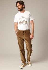 Bordeaux corduroy broek met een tailleband met trekkoord, gecombineerd met een witte graphic t-shirt met motorontwerp en casual sneakers.