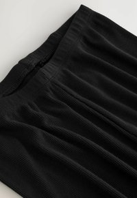 Čierny ryhovaný textil s jemným, elastickým pásom a subtílnymi záhybmi, s hladkým povrchom a prešívaním pozdĺž okraja.
