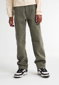 Olijfgroene katoenen broek met een relaxte pasvorm, voorzien van zijzakken en een gladde textuur, gecombineerd met zwart-witte sneakers.