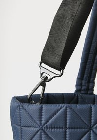 Tote torba od navy tkanine s kviltanim uzorkom, opremljena teksturiranim crnim remenom i crnom metalnom kopčom, s geometrijskim dijamantnim uzorcima.