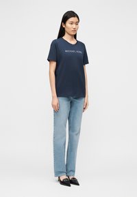 T-shirt de algodão azul-marinho com decote redondo e "MICHAEL KORS" bordado a branco. Combinado com jeans denim azul claro e sapatos de salto pretos.