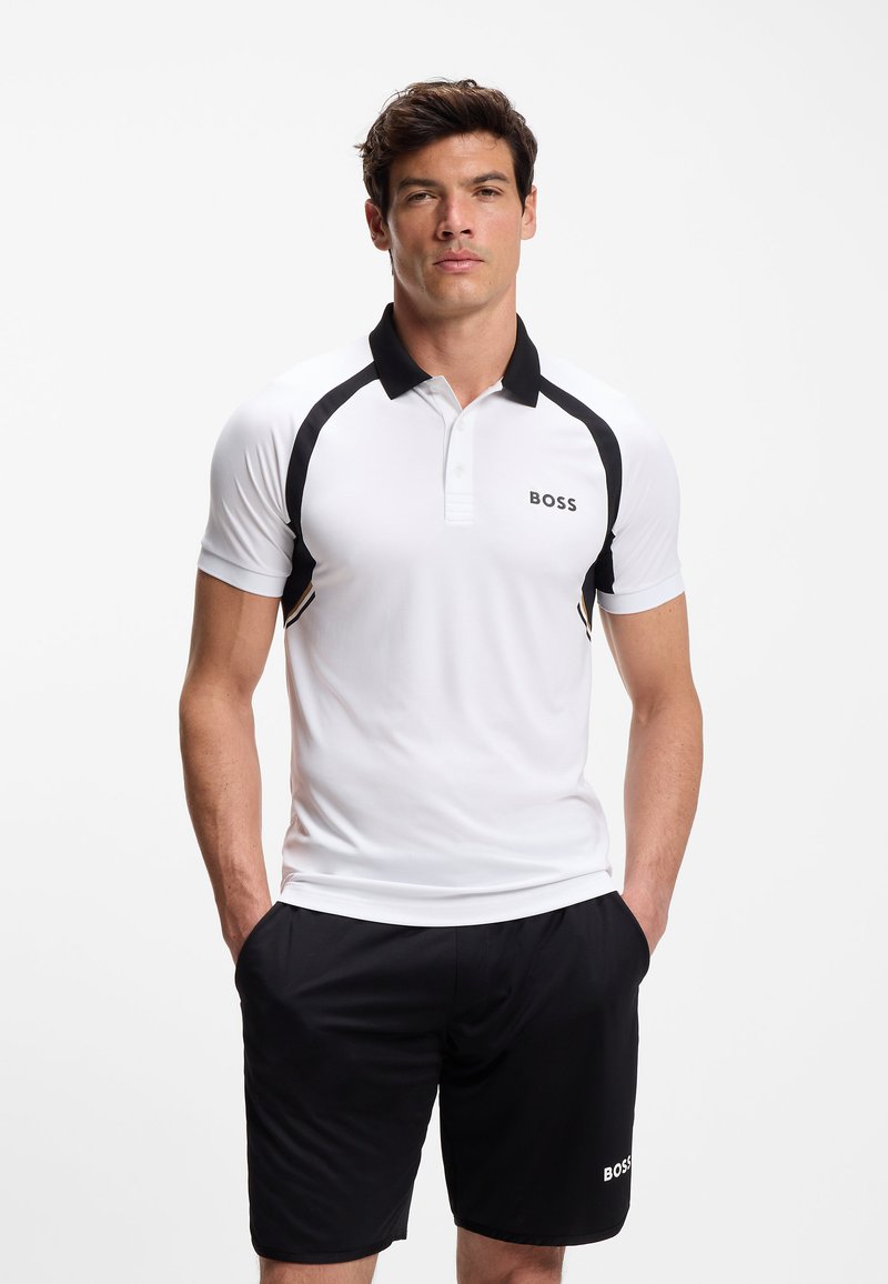 Weißes kurzärmeliges Polohemd mit schwarzen Akzenten und Kragen, mit "BOSS"-Logo. Kombiniert mit schwarzen Shorts, glattem Stoff und sportlicher Passform.
