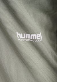 Hummel prestandakläder i ett strukturerat, ljust grönt tyg, med en framträdande vit logotyp på framsidan.