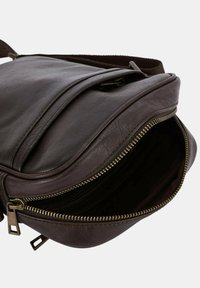 Sac en bandoulière en cuir marron foncé avec des compartiments zippés visibles et une sangle en tissu ajustable, présenté partiellement ouvert sur fond blanc.