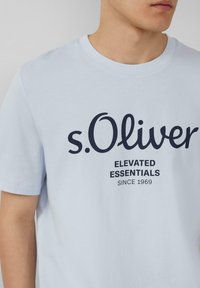 Lichtblauw katoenen t-shirt met een ronde hals en een zwart gedrukt logo met "s.Oliver" en tekst eronder, wat zorgt voor een contrast.