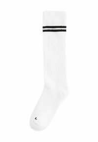 Chaussette blanche montante avec texture côtelée, présentant deux rayures noires horizontales en haut et un petit "L" imprimé sur le bout.
