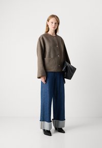 Brun uldblandet jakke, oversized pasform, frontknapper, to lommer. Kombineret med brede denim bukser med opkrøllede ben og sorte spidse støvler.