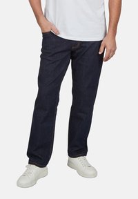 Vaqueros de mezclilla azul oscuro con corte recto, que presentan un diseño simple, costuras sutiles y se llevan con zapatillas blancas.