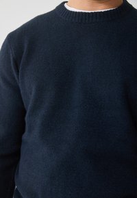 Dunkelblauer Strickpullover mit Rundhalsausschnitt und geripptem Kragen, aus einem weichen, strukturierten Stoff mit einem leicht flauschigen Aussehen.