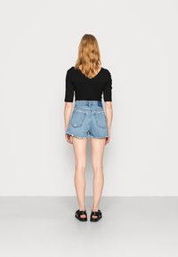 Top negro acanalado de manga corta, combinado con pantalones cortos de mezclilla azul con dobladillo deshilachado y bolsillos traseros, usado con sandalias negras.