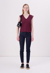 Burgundské tričko s výstřihem do V a krajkovými rukávy, doplněné tmavými džínami. Černá kabelka a tmavé tenisky dodávají outfitu finální úpravu.